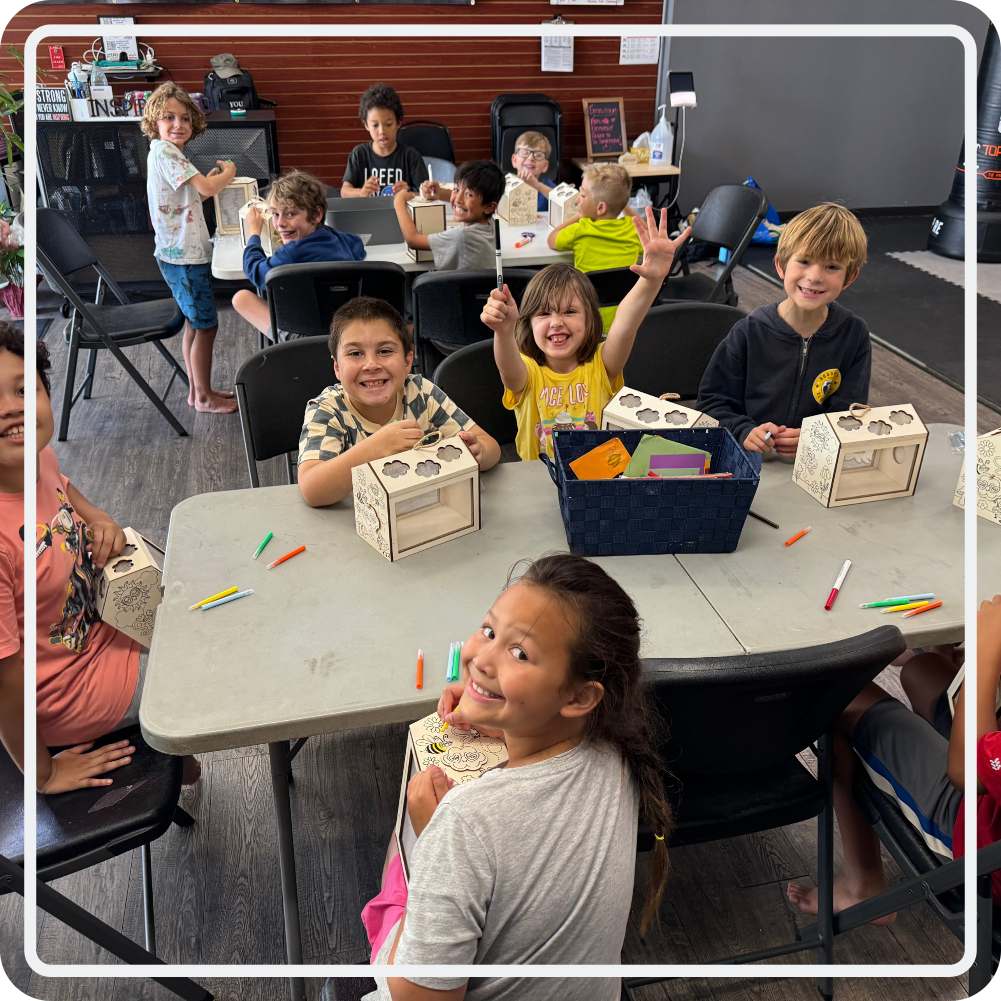 Children smiling and making craft projects together at tables inside Inspire